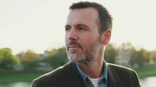 Close up, man looks around while sitting on the embankment on the background of the river