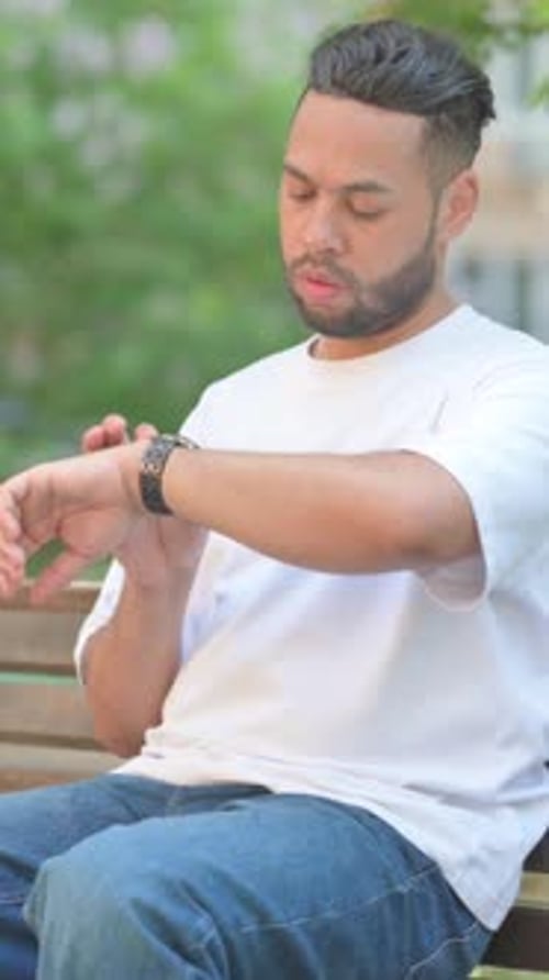 Young Man Checking Watch While Sitting on Bench
