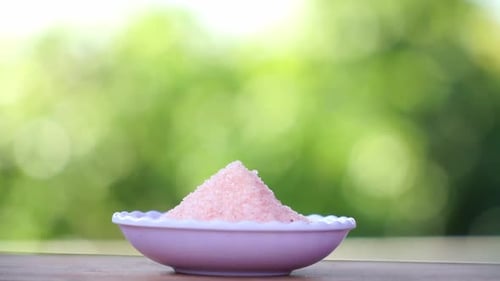A small bowl full of Himalayan salt with green blur nature background. Pink salt.