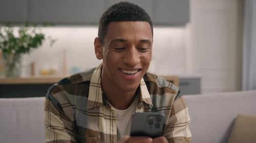 Young Man Smiling While Using Smartphone at Home