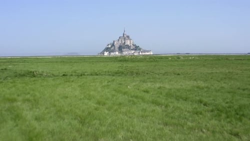 Low altitude flight towards Mont Saint-Michel across green grass fields.