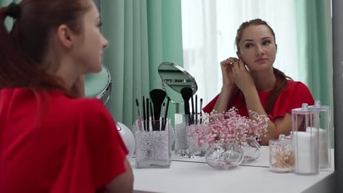 Woman Putting on Earrings at Vanity Mirror