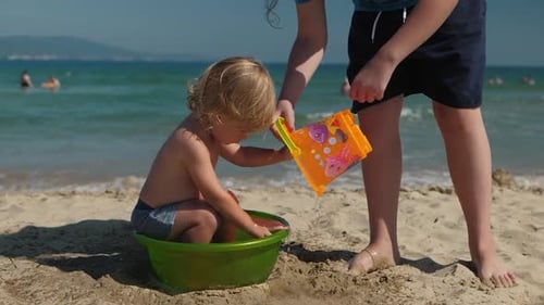 Niño pequeño en una bañera verde en la playa con un mayor