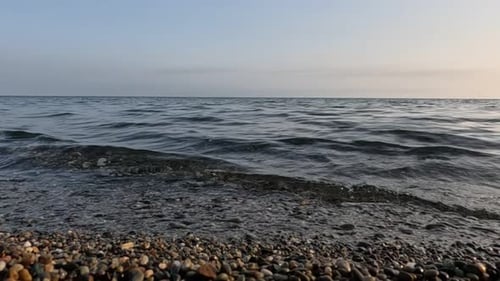 Meer, Strand, Horizont, Meereswellen mit weichem, schaumigem Wasser, das mehrfarbige Kieselsteine auf einem Strand wäscht, während