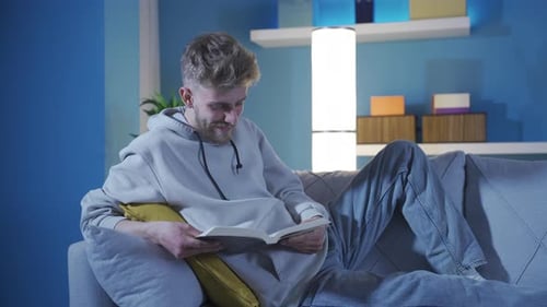 Glücklicher und gutaussehender junger Mann, der alleine zu Hause friedlich ein Buch liest.