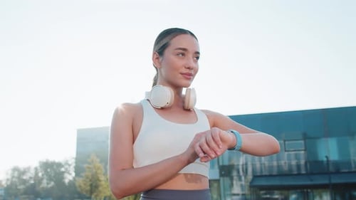 Young Female Runner Looks at Smartwatch Device Fitness Bracelet Heart Rate Pulse SPO2 in City Park