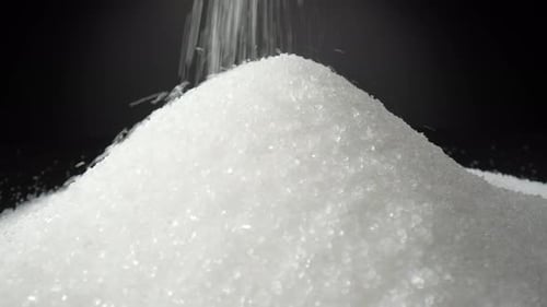 Weißer Zucker fällt zart auf einen glatten schwarzen Hintergrund