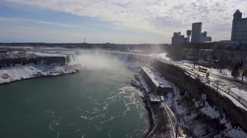 Aerial pan of misty Niagara Falls and city skyline in snowy winter