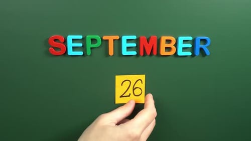 Hand sticking a sticker 26 September calendar day on school board. 26 date of September. Twenty
