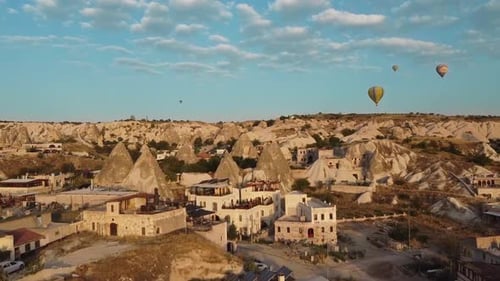 Flight over the houses of Goreme, with hot air balloons in the sky, in Cappadocia of Turkey