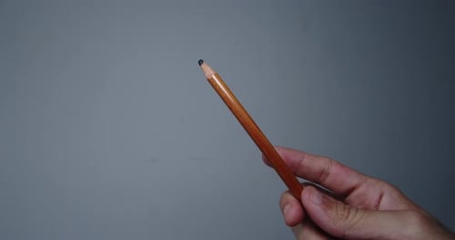 Pencil held by the hand of a young man showing it to the camera inside a room with white walls. 4K