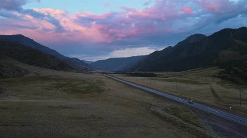 Aerial View of a Valley with a River and Road Surrounded By Mountains at Sunset