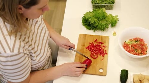 Frischer Gemüsesalat: Frau, die einen grünen Salat mit Gurken, Zwiebeln, Salat, Pfeffer und Tomaten zubereitet