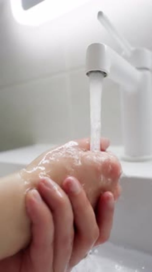 Woman Washing Hands Under Running Water in Bathroom