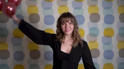 Woman Holding Red Balloons in Front of Patterned Wall