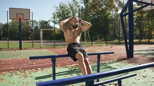 Shirtless Man Doing Sit-ups on Parallel Bars Outdoors