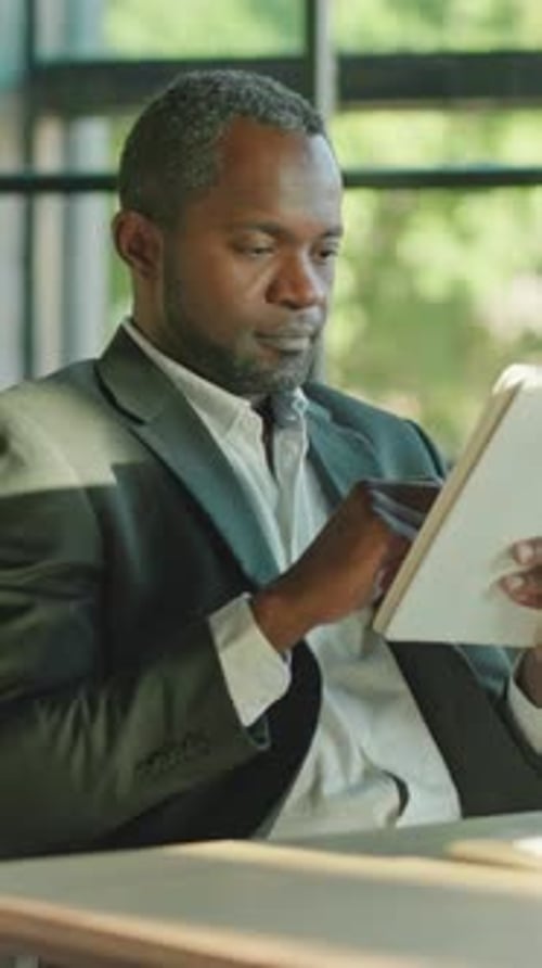 A Professional Man is Utilizing a Tablet While Seated in a Contemporary Workspace Environment