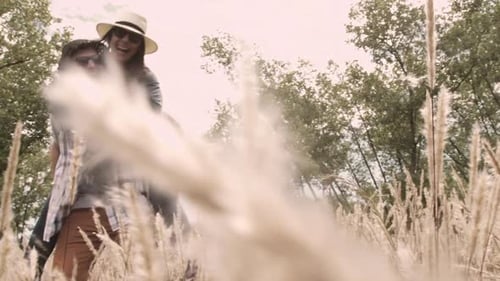 Young couple enjoying piggyback ride and laughing together in windy field