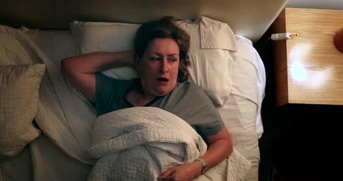 Mujer mayor que enciende la luz de la mesita de noche y se levanta de la cama en mitad de la noche