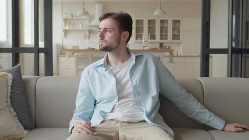 Man Sitting on Couch Turns on TV