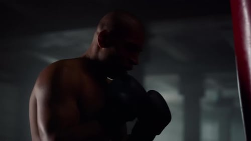 African american boxer punches bag with power in dark gym prepares for fight