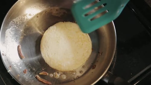 Flipping Hot Pancake In A Stainless Pan With Melted Butter Using A Green Spatula - Closeup Shot