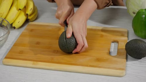Hands Prepare an Avocado on Cutting Board