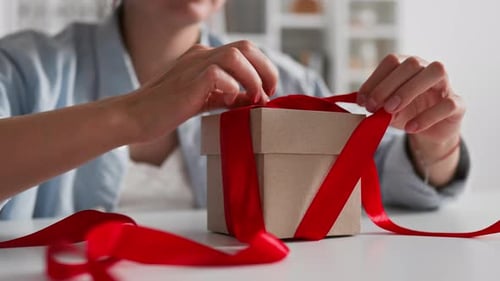 Woman Tying Red Bow and Opening Gift