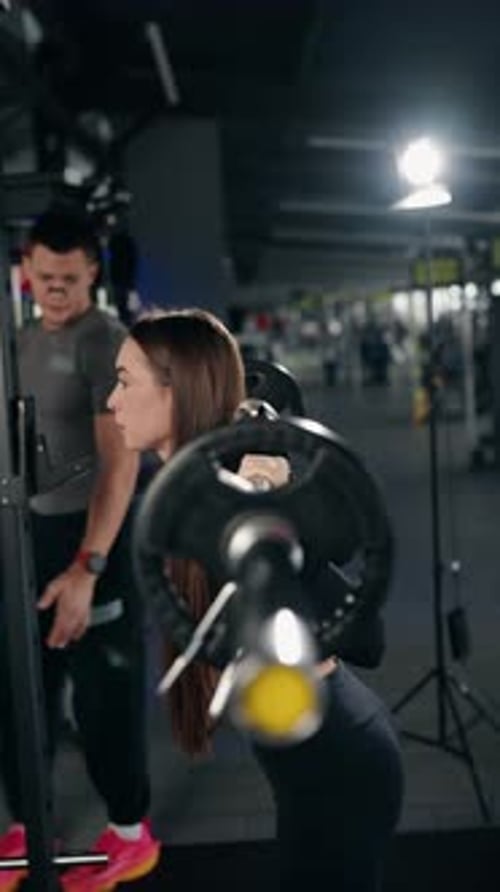 Woman Doing Barbell Squats With Personal Trainer in Gym