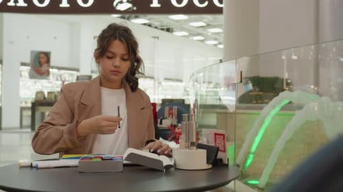 Chercheuse d'un café dans un centre commercial, une femme blanche feuillette un livre de référence et note des mains concentrées