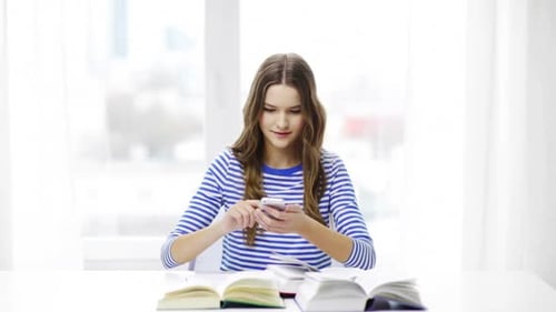 Teenage girl studying with phone at table indoors