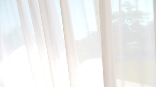 Light Breezy Sheer Curtain Blowing in the Wind with Garden Behind It