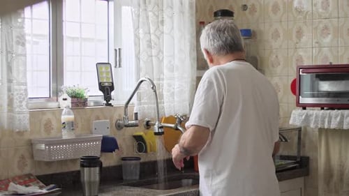 Senior Man Filling Sink with Water in Kitchen