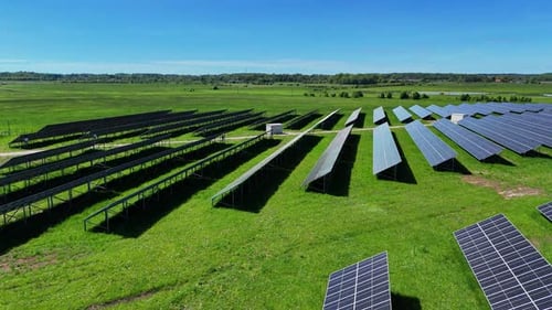 A large solar panel field in a lush green landscape under a clear blue sky, aerial view