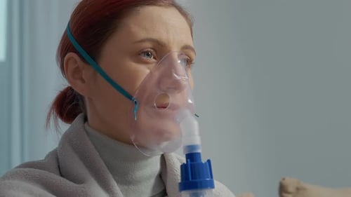 Femme assise sur un canapé utilisant un nébuliseur pour un traitement respiratoire à l'intérieur