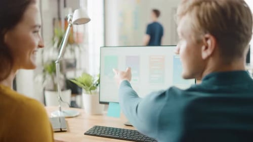 Três desenvolvedores de software móvel trabalham em computadores desktop e discutem o design de aplicativos para smartphones