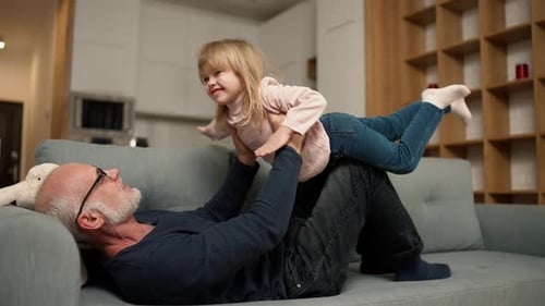 Grandfather and Granddaughter Play Airplane on Couch