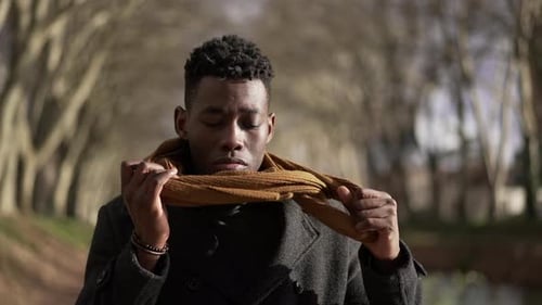 Man in Coat Adjusts Scarf Outdoors in Sunlight