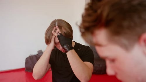 Athlete in Black Sportswear Sits on Red Mat Inside Gym Looking with Focused Expression