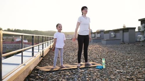 Mother and Daughter Exercising Squats Together Outdoors on a Sunny Rooftop
