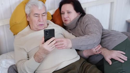 Senior Couple Relaxing in Bed with Smartphone