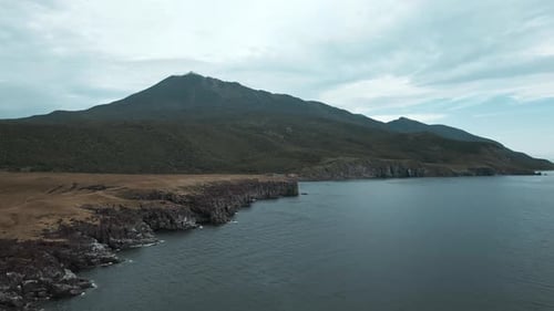 Top view of rocky coast on background of mountains on cloudy day