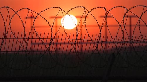 Barbed Wire Fence Silhouetted Against Fiery Sunset