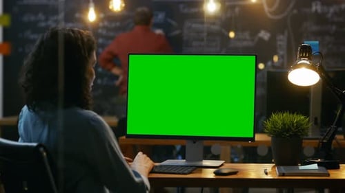 Beautiful Female Office Employee at Her Desktop Works on a Mock-up Green Screen Personal Computer.