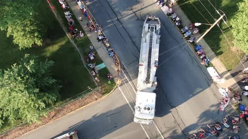 Aerial top down birds eye view of firetruck and police car in Fourth of July Parade, crowds line str