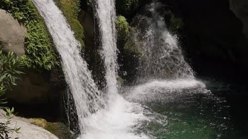 Twin Waterfalls Cascading Over Moss-Covered Rocks Into A Pool Below. Lush Greenery Surrounds.