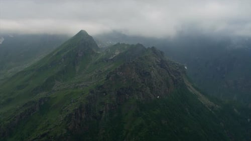 Green mountaintops under cloud layer with small paraglider