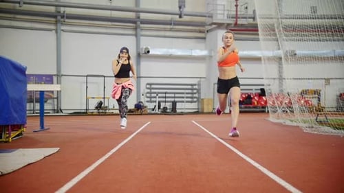 Two Female Athletes Running Together on Indoor Track