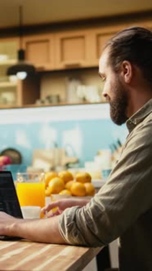 Vertikales Video: Eine Person beim Programmieren auf einem Laptop in einer Küche, das Telearbeit in der IT darstellt