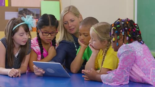 Teacher And Group Of Students Look At Digital Tablet Together In School Classroom